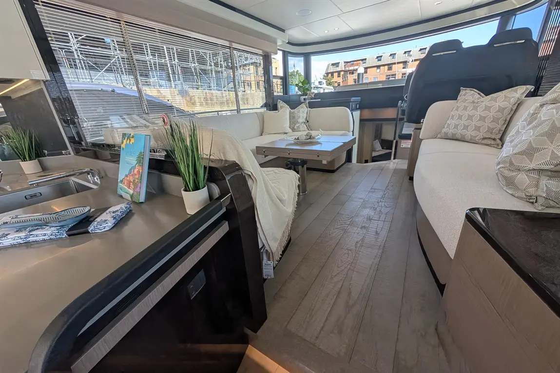 Luxury yacht interior featuring a modern lounge, kitchenette, patterned cushions, plants, and a scenic view through large windows.